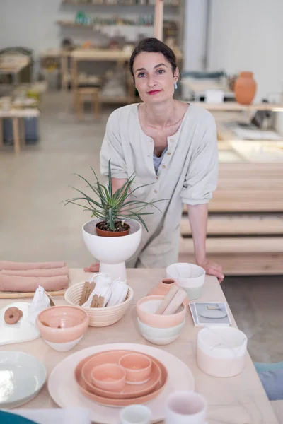 Beautiful happy craft woman wearing apron looking at camera and smiling while standing in her art studio