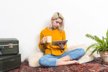 Oturma odasında yerde otururken tabletini kullanan bir kadın.