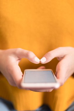 Sarı kazaklı, akıllı telefon kullanan bir kadının yakın çekimi.