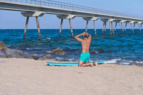 男はビーチでひざまずきながらサーフィンの準備 — ストック写真