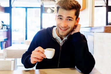 Gülümseyen yakışıklı kahveci modern kafe içinin barında kahve ile oturuyor.