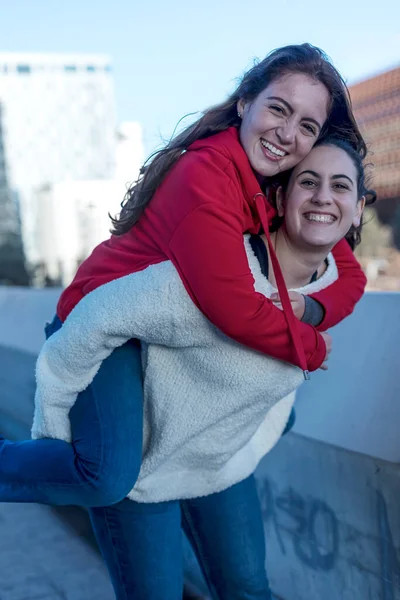 stock image Half length of two blonde and redhead women friends having fun outdoor in the city, riding piggyback - happiness, friendship, having fun concept