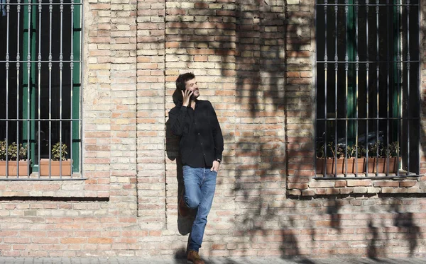 Güneşli bir günde duvara yaslanırken cep telefonuyla konuşan kendine güvenen bir adam.