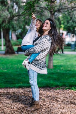 Anne kızını kucağında tutuyor ve güzel bir sabahta parkta oynuyor..