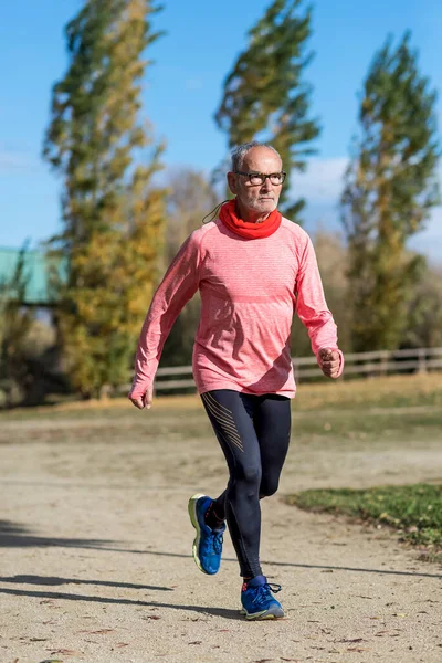Siyah ve yeşil giyinmiş son sınıf öğrencisi parkta koşuyor.