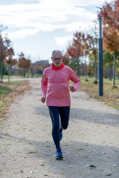 Siyah ve yeşil giyinmiş son sınıf öğrencisi parkta koşuyor.