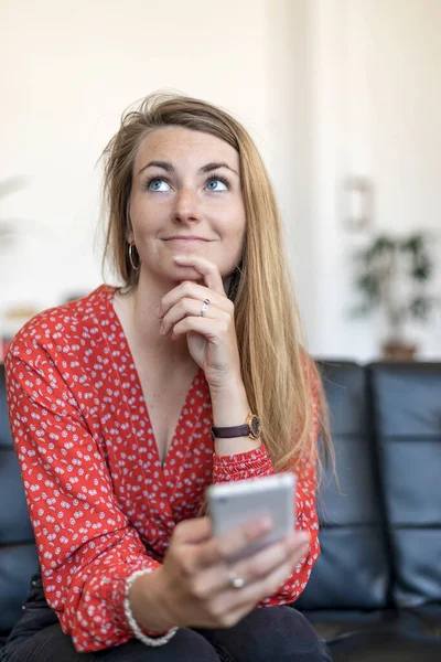 Hermosa Mujer Caucásica Sostiene Teléfono Celular Mano Sienta Sofá Mientras — Foto de Stock