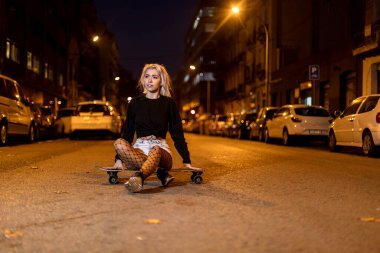 Şehirde gece kamera bakarken uzun bir tahta üzerinde şort genç kadının ön görünümü