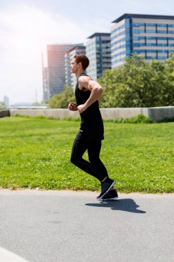 Gün batımında şehirde koşan yakışıklı bir sporcunun yan görüntüsü