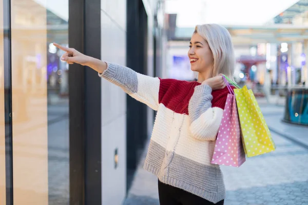 路上のショッピングモールを指す買い物袋を持つ若い幸せな笑顔の女性の肖像画 — ストック写真