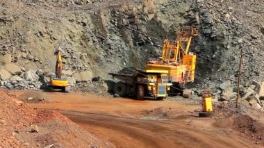 Taş ocağında demir cevheri çıkarma işlemi. Demir madenini açık bir çukura boşaltmak için gerekli ekipman. Demir cevheri ocağındaki akıllı işlem. Taş ocağındaki bir kazıcı bir çöp kamyonuna toprak yüklüyor..