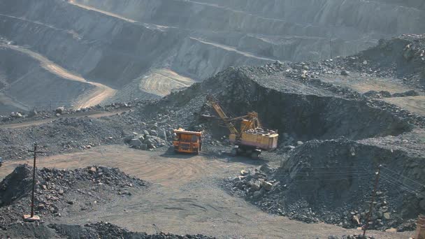 Uma escavadora numa pedreira carrega o solo num camião. O processo de mineração de minério de ferro em uma pedreira. Equipamento para a extracção de minério de ferro num poço aberto. O processo inteligente em uma pedreira de minério de ferro — Vídeo de Stock