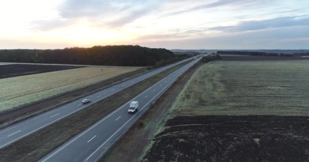 Ciężarówka odjeżdża prosto w stronę zachodzącego słońca. Ciężarówka jedzie wzdłuż drogi między polami o zachodzie słońca — Wideo stockowe