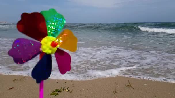 Barnväderkvarn till havs. Barnväderkvarn. En färgglad barnväderkvarn snurrar på stranden. — Stockvideo