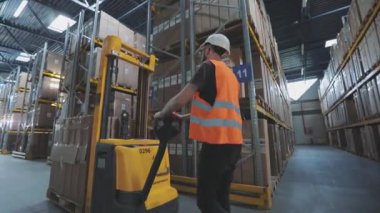 Elektrikli forklifti olan bir işçi. Depoda işçi forklifti var. İşçi depoda yürüyor.