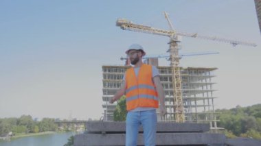 Bir mühendis inşaat alanında sevinir. Mühendis inşaat alanında neşeyi canlandırıyor. İnşaat alanında genç bir mühendis ellerini kaldırıyor.