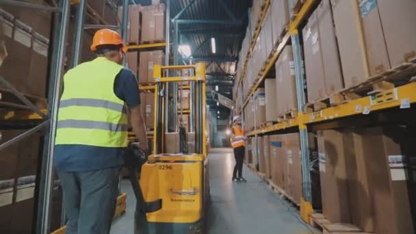 Depoda çalışan bir işçi elektrikli forklift taşır. Depoda forklift kullanan bir işçi. İşçi depoda yürüyor. — Stok video