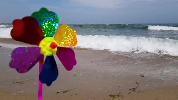 Barnväderkvarn på havet. En väderkvarn för barn i vinden, en färgad väderkvarn för barn snurrar från vinden på stranden. — Stockvideo