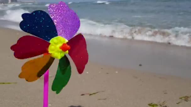 En färgglad barnväderkvarn snurrar på stranden. Barnväderkvarn till havs. Väderkvarn för barn — Stockvideo