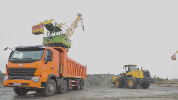 Погрузка грузовика в порт, портовые краны, экскаватор загружается в материал в грузовике — стоковое видео