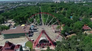 Parkta dönme dolap, hava manzaralı. Yeşil bir parkın ortasında İHA 'yla çekim yapan büyük bir dönme dolap.