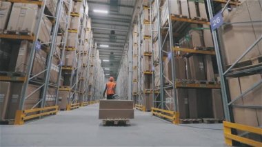 Turuncu yelekli bir adam depoda kutu taşıyor. Fabrikada iş gününün sonunda. Depodaki ışıkları kapatıyorum.