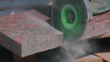 Bir işçi granit levhayı öğütücüyle keser. İnşaat alanında çalışma süreci. İnşaat alanında öğütücü olarak çalışıyorum.