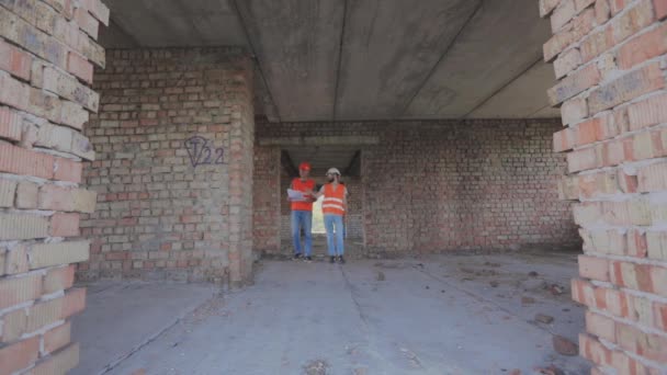 Deux ouvriers en uniforme sur un chantier. Deux constructeurs dans la maison. Ingénieurs à la construction d'immeubles d'habitation. — Video