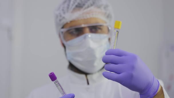 El científico mira los tubos de ensayo para el plan. Tubos de ensayo de laboratorio de cerca, la cara del científico en el fondo — Vídeo de stock