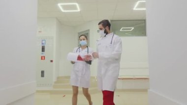 Doktorlar hastanenin parlak modern koridorları boyunca yürürler. Antiviral korumadaki doktorlar parlak hastane koridorlarında yürüyorlar.