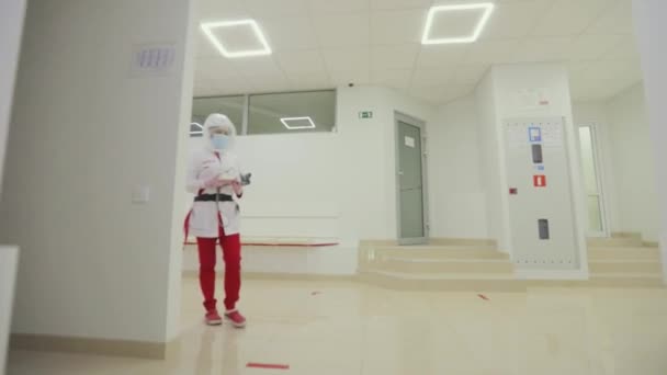 La femme médecin marche dans le couloir des lames. Un travailleur médical marche le long du couloir lumineux de la clinique, tient du matériel médical dans ses mains — Video