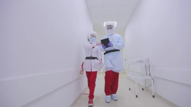 Los médicos caminan por los luminosos y modernos pasillos del hospital. Los médicos en protección antiviral están caminando a lo largo de los corredores brillantes del hospital — Vídeos de Stock
