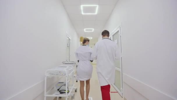 Лікарі ходять по світлих сучасних коридорах лікарні. Лікарі в антивірусному захисті ходять по яскравих лікарняних коридорах — стокове відео
