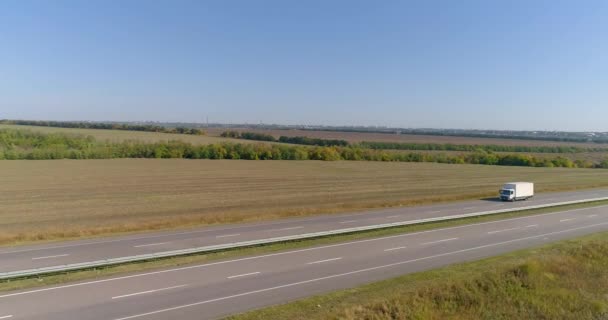 天気の良い日には白いワゴンが高速道路を走っている。天気の良い日にはトラックが高速道路を走る。ワゴンは美しい道路に沿って運転しています — ストック動画