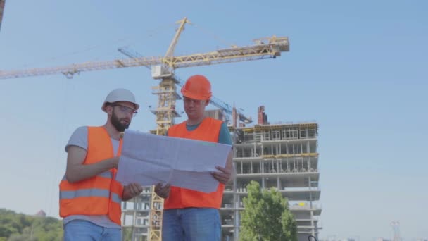 Ingegneri di fronte a un edificio a più piani. Due ingegneri di un cantiere stanno guardando il disegno. Due costruttori sullo sfondo della casa — Video Stock