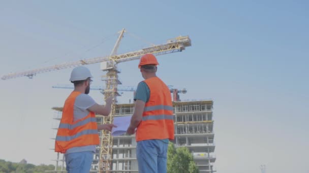 Ingegneri di fronte a un edificio a più piani. Due ingegneri di un cantiere stanno guardando il disegno. Due costruttori sullo sfondo della casa — Video Stock