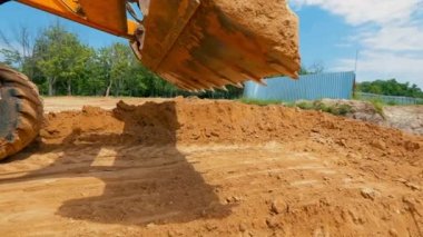 Traktör kovası yaklaş. Bir traktör inşaat alanında çukur kazıyor. İnşaat alanında çalışma süreci.