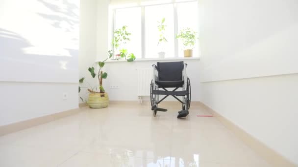 Rolstoel in de gang van de kliniek. De camera zoomt uit de lege rolstoel voor gehandicapten. Een frame dat verlies simuleert — Stockvideo