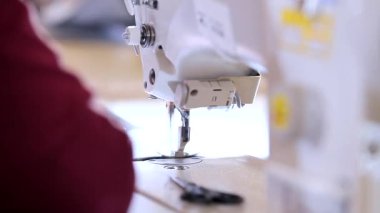Bir terzi dikiş makinesine yakın çekim sırasında sıra oluşturur. Dikiş fabrikasındaki dikiş işlemine yakın çekim. Profesyonel ekipmanlarda dikiş işlemi.