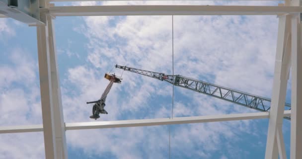 Construction crane on a background of blue sky with clouds. The hook of the construction crane hangs above the camera — Stockvideo
