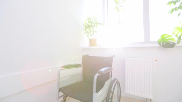 Pusty wózek inwalidzki dla osób niepełnosprawnych w korytarzu szpitala. Wózek inwalidzki dla niepełnosprawnych w białym korytarzu. Pusty wózek inwalidzki na tle jasnego okna — Wideo stockowe
