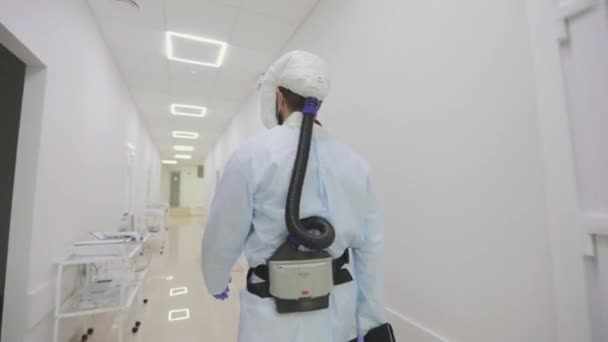 A doctor in a protective suit walks down the hospital corridor, rear view. A doctor in a protective suit, a view from the back.The doctor walks along the corridor of the modern clinic — ストック動画