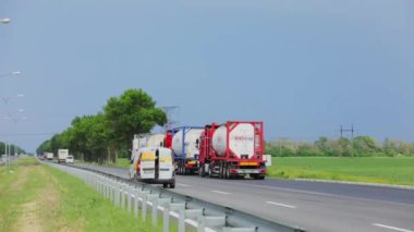 Kamyonlar yol boyunca gidiyor. Bir kamyon konvoyu otobanın altından geçiyor. Pistteki modern kamyonlar