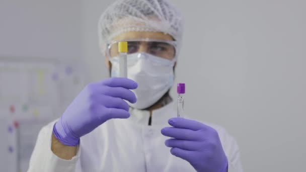 The laboratory assistant examines the test tubes close-up. Male laboratory assistant examines test tubes in the laboratory — Wideo stockowe