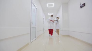 Antiviral korumadaki doktorlar parlak hastane koridorları boyunca yürüyorlar. Doktorlar hastanenin parlak modern koridorlarında yürürler.