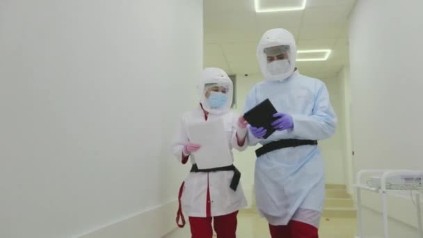 Лікарі в антивірусному захисті ходять по яскравих лікарняних коридорах. Лікарі в захисних костюмах ходять по лікарняних коридорах . — стокове відео
