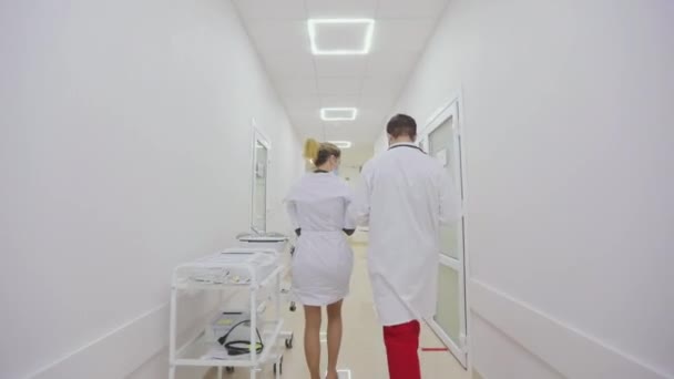 Врачи в защитных костюмах ходят по коридорам больницы. Врачи в антивирусной защите идут по светлым коридорам больницы — стоковое видео