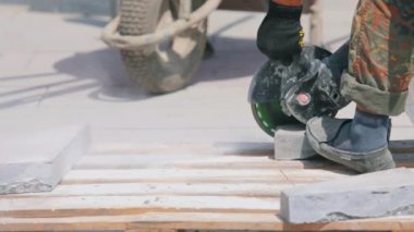Bir işçi granit levhayı öğütücüyle keser. İnşaat alanında çalışma süreci. İnşaat alanında öğütücü olarak çalışıyorum.