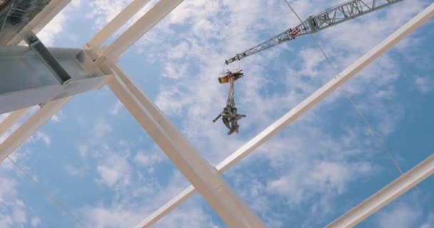 Construction crane on a background of blue sky with clouds. The hook of the construction crane hangs above the camera. Bottom view of a tower crane. — стоковое видео