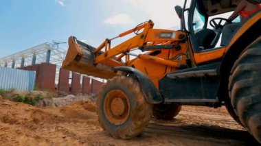 Büyük sarı bir kazıcı bir inşaat alanında araba sürüyor. Kazı tekerleri kapanıyor.